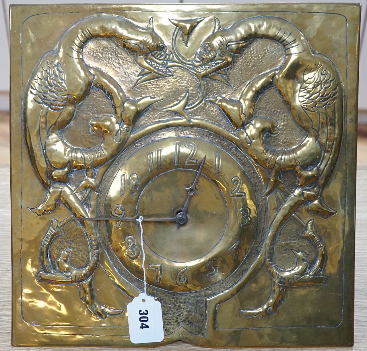An early 20th Century Arts & Crafts/Art Nouveau brass wall clock in the manner of Margaret Gilmour, Glasgow School with embossed weights and pendulum, dial 37x37cm, Black Forest type movement